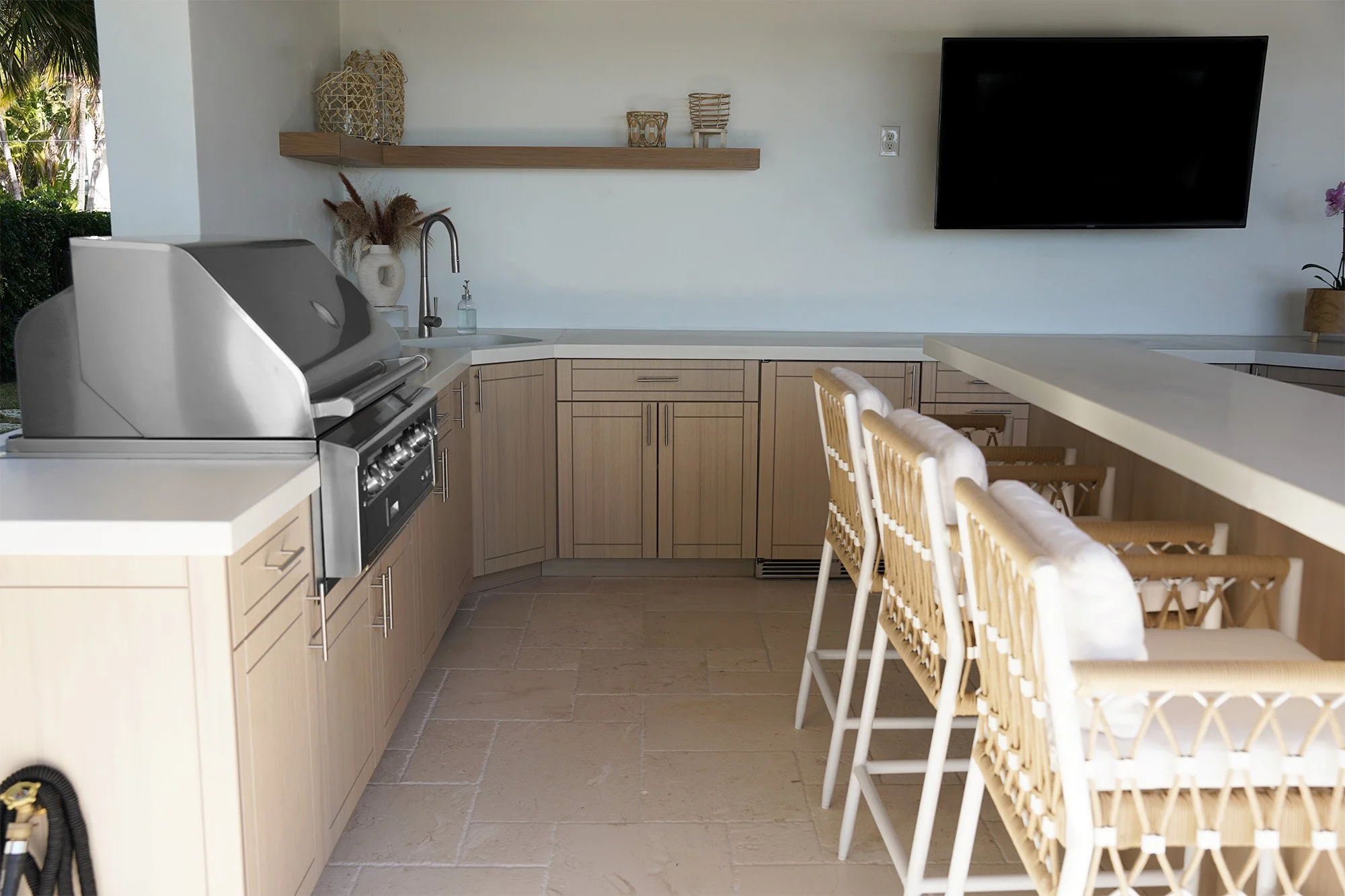 Light wood outdoor kitchen with a built-in grill, prep sink, and bar seating.